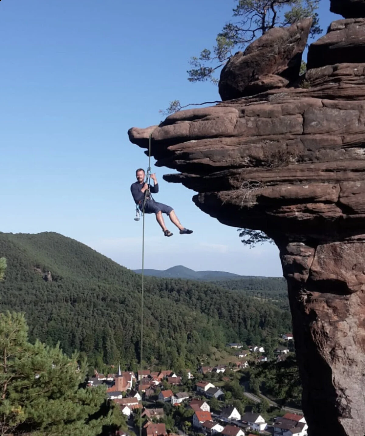 Eine Person seilt sich an einem Kletterseil von einem Felsen ab. Im Hintergrund ist ein Wald und ein Dorf zu sehen. | © DAV Kaiserslautern_Philipp,Krumm