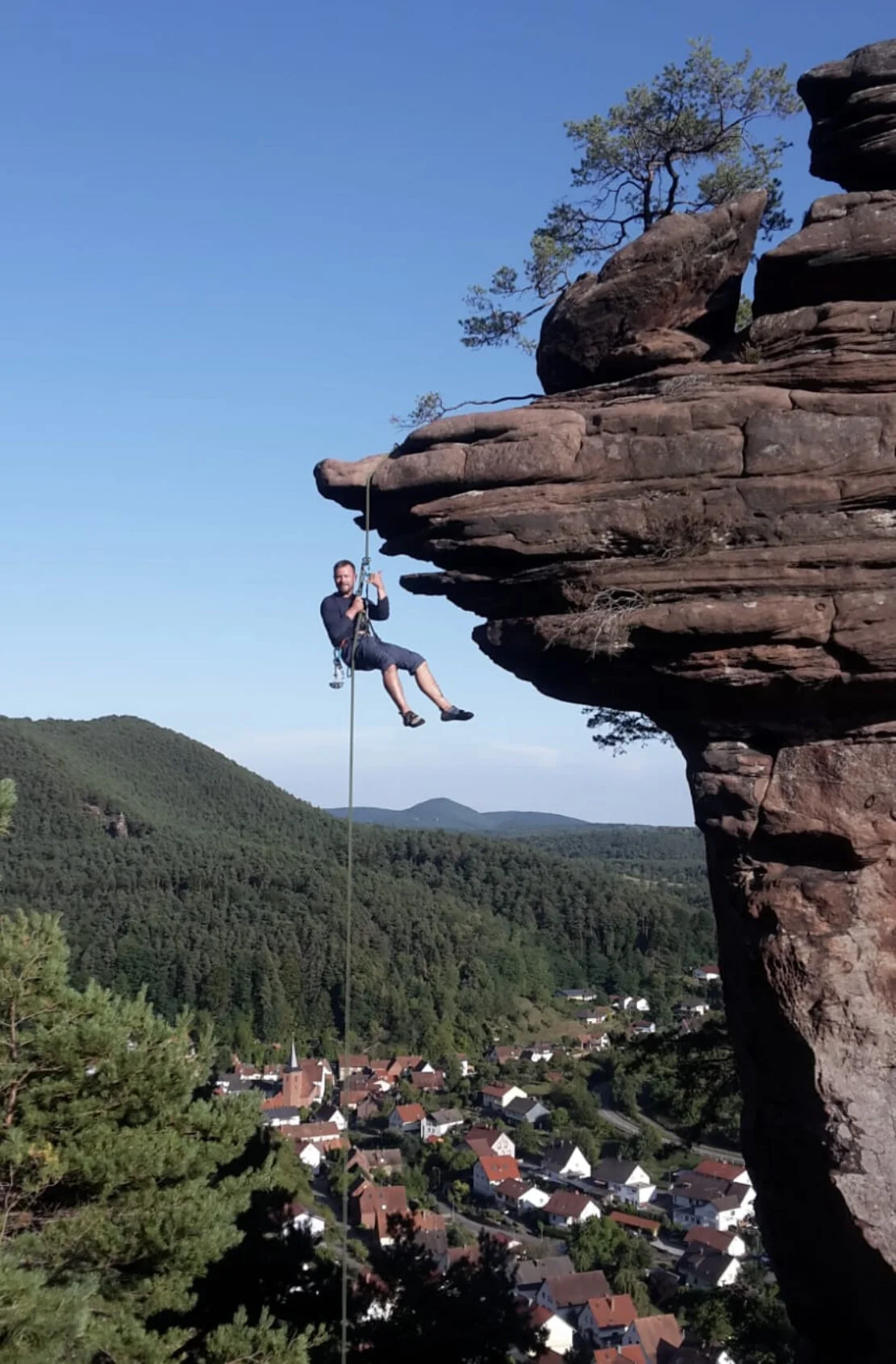 Eine Person seilt sich an einem Kletterseil von einem Felsen ab. Im Hintergrund ist ein Wald und ein Dorf zu sehen. | © DAV Kaiserslautern_Philipp,Krumm