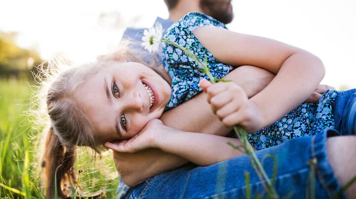 Ein Mädchen mit ihrem Vater auf einer Frühlingswiese | © Halfpoint / Adobe Stock